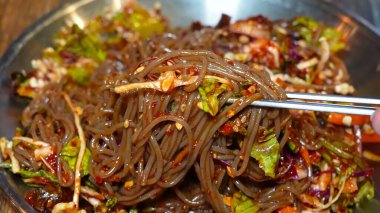 Bir tabak taze soba eriştesi, otlar, sebzeler, susam tohumları ve parlak bir sosla süslenmiş..