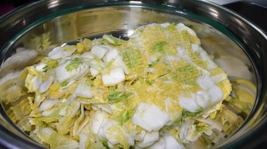 Eldivenli bir şef, sağlıklı bir yemeğe hazırlanmak için çelik bir kasede taze Çin lahanası yaprakları kesiyor..