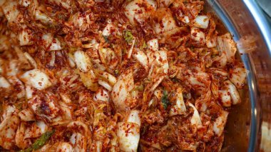 Eldivenli bir el, Çin lahanasını domates sosu ve aromatik baharatlarla büyük bir metal kasede ustalıkla karıştırıyor..