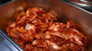 Eldivenli bir el, Çin lahanasını domates sosu ve aromatik baharatlarla büyük bir metal kasede ustalıkla karıştırıyor..