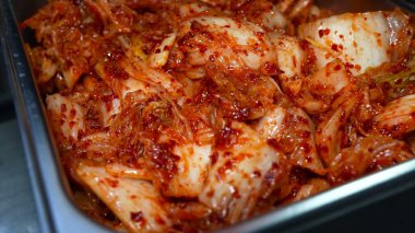 Eldivenli bir el, Çin lahanasını domates sosu ve aromatik baharatlarla büyük bir metal kasede ustalıkla karıştırıyor..