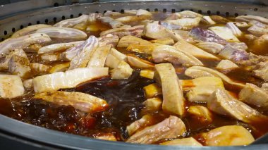 Domuz kaburgaları endüstriyel ölçekte büyük tavalarda pişiriliyor, zengin bir et suyunda kaynıyor..