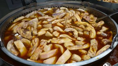 Domuz kaburgaları endüstriyel ölçekte büyük tavalarda pişiriliyor, zengin bir et suyunda kaynıyor..