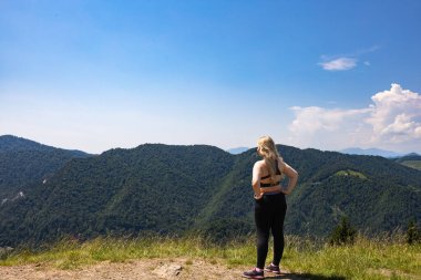 Tepede duran ve dağlara bakan kadın.