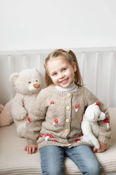 Baby knitted clothes. Handmade knitted sweater with fly agaric mushrooms. Jacket with embroidery. Child girl at home.
