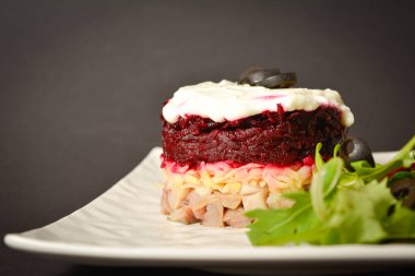 Close up to Soviet layered fish salad Herring under fur coat. Portion with marinated herring, onion, grated potato, beetroot, mayonnaise on top with lettuce olive salad. Dark copy space background