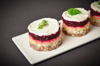 Top view of Traditional holiday layered fish salad Herring under fur coat served in culinary rings. serving size of salad with marinated herring fish, onion, grated potato, beetroot, mayonnaise on top