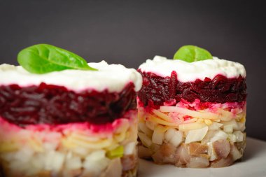 Close up to traditional layered fish salad with beetroot, potato, onion, herring and mayonnaise. Salad herring under fur coat served in culinary rings in focus and out of focus on dark background