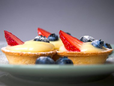 Side view of little crusty French tarts filled with custard cream and fresh strawberries and blueberries