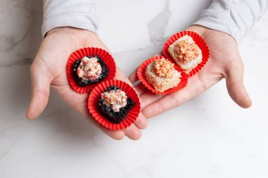 Man holds sushi different roll pieces in hands. Sushi in paper pack. Black and white rice sushi roll pieces with salmon and eel. Holding sushi on light background