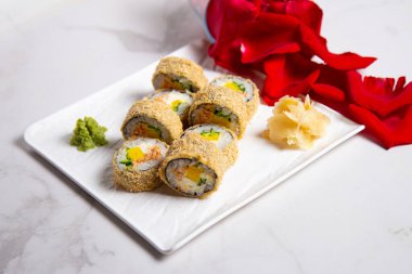 Close up to hot tempura sushi roll with salmon. Red rose petals near served dish on marble background. Breaded Sushi roll portion with ginger and wasabi on white marble background