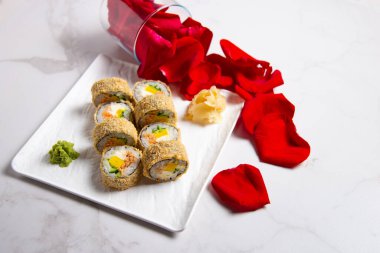 Somonlu sıcak tempura suşinin en üst görüntüsü. Kırmızı gül yaprakları mermer arka planda servis edilen yemeğin yanında. Beyaz mermer arka planda zencefil ve wasabi soslu haşlanmış suşi.