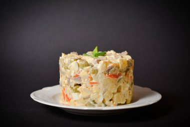 Olivier 'in beyaz tabakta servis ettiği geleneksel Rus salatasının yan görüntüsü. Patates ve havuç küplü salata, yeşil bezelye, salatalık turşusu, koyu arkaplanda taze soğanlı yumurta.