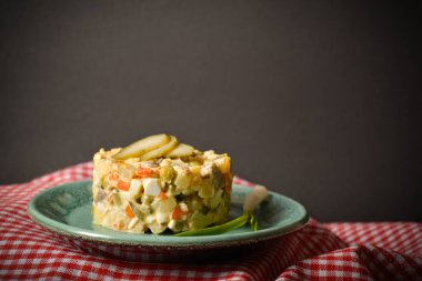 Side view of traditional rustic salad Olivier served in culinary rings Country Salad with potato, carrot, green peas, pickled cucumbers, eggs on American red checkered kitchen towel, black background