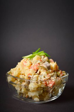 Geleneksel Rus salatasına yakın, Olivier siyah kutunun üzerindeki cam kasede servis ediliyor. Patates ve havuç küplü salata, yeşil bezelye, salatalık turşusu, koyu arkaplanda yumurta.