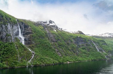 Norveç, Geiranger fiyordunda karlı dağ zirveleri ve şelaleleri olan güzel bir manzara.