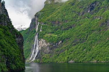 Norveç, Geiranger fiyordunda karlı dağ zirveleri ve şelaleleri olan güzel bir manzara.