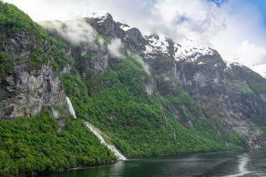 Norveç, Geiranger fiyordunda karlı dağ zirveleri ve şelaleleri olan güzel bir manzara.