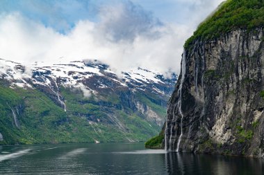 Norveç, Geiranger fiyordunda karlı dağ zirveleri ve şelaleleri olan güzel bir manzara.