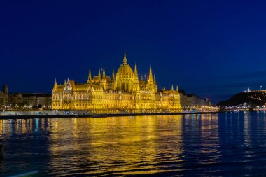 The Budapest Parliament building at night, with the Danube in the foreground