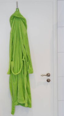 Yeşil bornoz beyaz bir odada asılı.