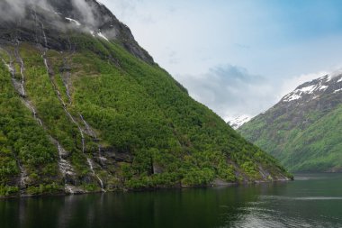 Norveç, Geiranger fiyordunda karlı dağ zirveleri ve şelaleleri olan güzel bir manzara.