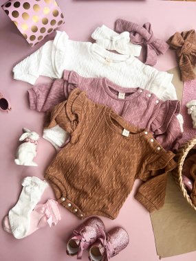 Bebek kıyafetleri, aksesuarlar, pastel arka planda elbise ve patiler. Yeni doğanlar için moda öğeleri, üst görünüm.