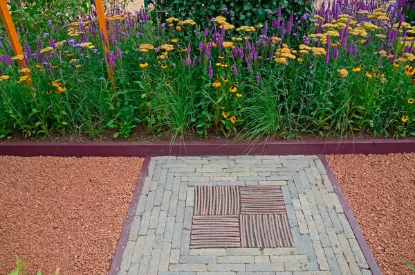 stock image A close up garden view with a decorative mosaic stone insert by a border of Achellia, Verbena and Veronica Purpleicious