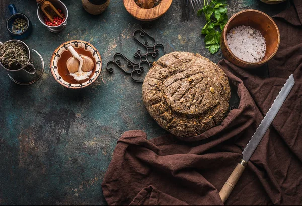 stock image Homemade whole grain bread on dark kitchen table background with knife and cooking tools and ingredients. Top view. Place for text