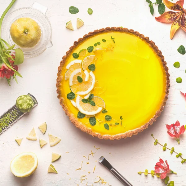 黄色のレモンタルトに柑橘類の成分と花 トップビューで白いテーブルの背景に新鮮なレモンとライムスライスがトッピングされています 伝統的なフランス料理 — ストック写真