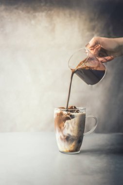 Barista el, beton arka planda, kırsal masanın üzerine buzlu kahve fincanı içine kahve kreması döküyor. Buzlu kahve yapmak. Yaz ferahlatıcı içecek. Soğuk içecek. Buzlu kahve..