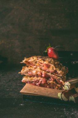 Koyu mutfak masasında ev yapımı robarb çilekli kek parçaları. Mevsimlik hamur işleri