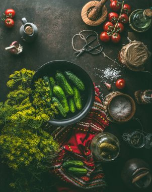 Salatalık reçeli. Taze salatalıklı, dereotlu ve baharatlı bir kâse koyu rustik mutfak masası arka planında, çatal bıçak ve salatalık kavanozu, üst manzara. Sağlıklı mayalanmış gıda konsepti