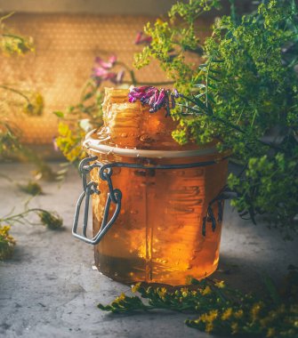 İçinde yabani çiçekler ve koyu beton arka planda bal petekleri olan bir kavanoz taze bal. Doğal ürünlerle sağlıklı beslenme. Ön görünüm