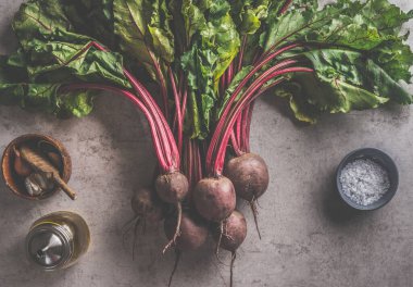 Yeşil yapraklı taze pancar kökü ve yemek malzemeleri: koyu beton arka planda zeytin yağı, tuz ve sarımsak. organik sebze. Sağlıklı gıda konsepti. Üst görünüm