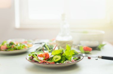 Plate with fresh green salad and fork on table at sunny kitchen background. Healthy eating. Dieting food. Lunch