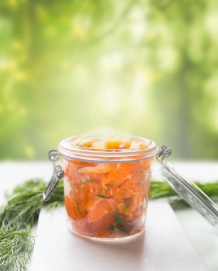 Slices of homemade smoked salmon with dill and lemon in glass jar on table at blurred nature background. Healthy food concept. Home cuisine recipes