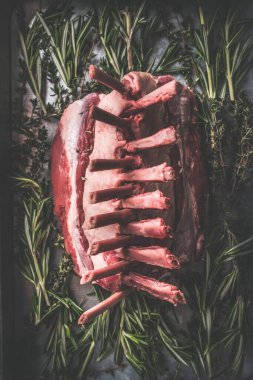 Close up of raw lamb racks preparation on dark rustic kitchen table background with herbs und spices. Top view. Raw meat food. Lamb crown roast making