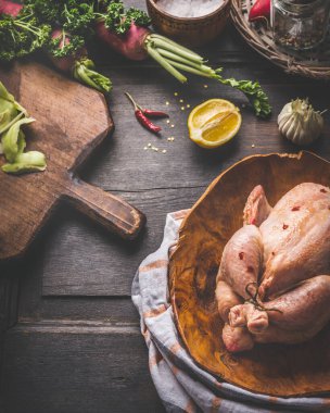 Chicken cooking concept. Raw whole chicken in wooden dish with ingredients on rustic background. Close up