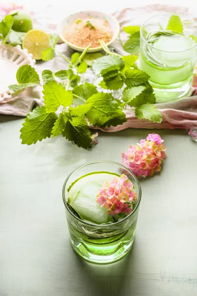 夏天清爽的饮料 茶杯中的绿色饮料 黄瓜和香草放在轻便的桌子背景上 配以可口的柠檬水或倒入水中 — 图库照片