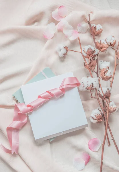 带有笔记本 白色盒子 粉色缎带 米色面料背景 棉枝和粉色花瓣的审美生活方式 顶部视图 — 图库照片