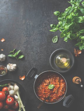 Lezzetli sos bolonez, siyah bir tavada, koyu renk mutfak masasında taze malzemeler ve zeytinyağıyla birlikte fesleğen ve kaşık yapraklarıyla evde yapılır. Yukarıdan bak. Çerçeve. Gıda arkaplanı