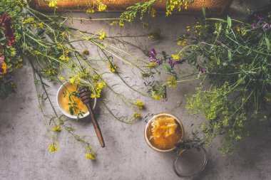 Farklı kavanozlarda bal kaşığı ve koyu beton arka planda yabani çiçekler olan doğal bal. Doğal ve sağlıklı gıda konsepti. Üst görünüm