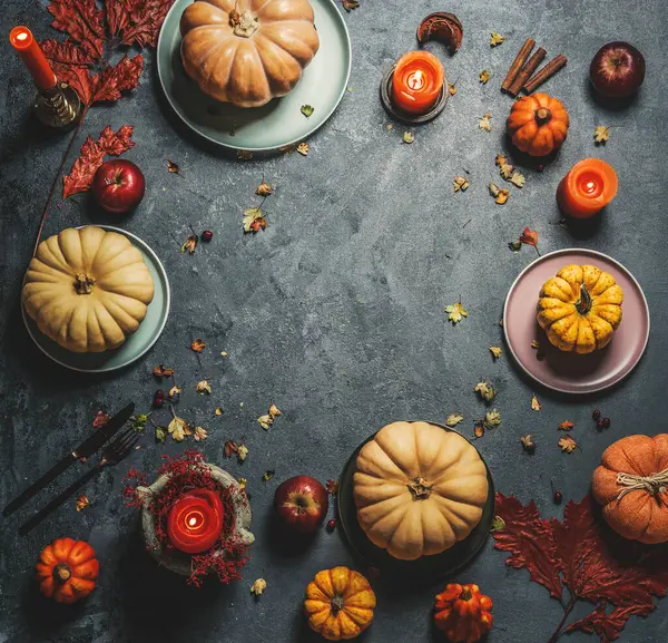 Turuncu mumları, çatal bıçak takımları ve koyu kırsal arka planda sonbahar yaprakları olan çeşitli kabaklar. Üst Manzara. Çerçeve