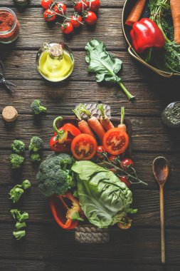 Ahşap tabakta çeşitli renkli sebzeler, mutfak aletleri ve malzemeler: lahana, domates, brokoli, havuç, dolma biber, kırsal ahşap mutfak masasında zeytin yağı. Üst Manzara. Sağlıklı yemek.