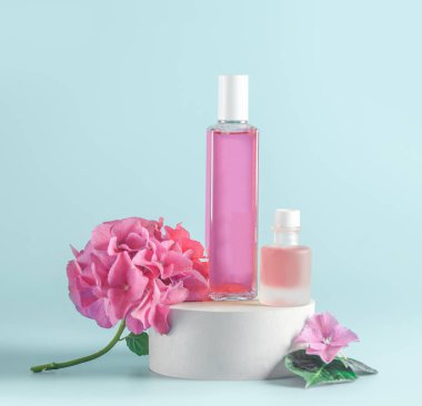 Açık mavi arka planda ortanca çiçekli kozmetik ürünleri sunumu. Kürsüde pembe sıvılı cam şişeler ve taç yaprakları. Ön manzara. Boşluğu kopyala.