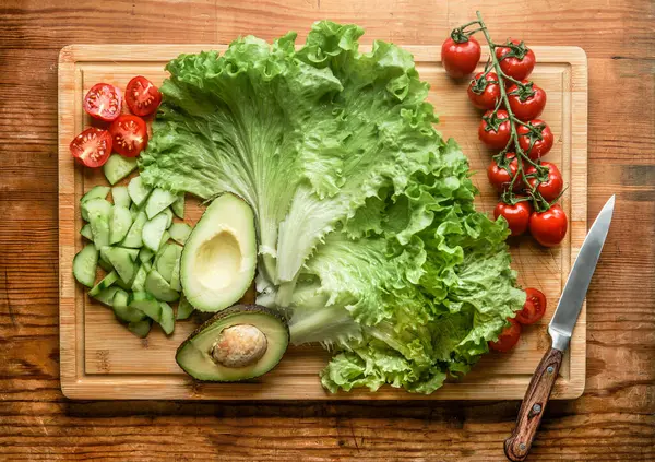 健康的な新鮮なサラダの原料 レタス 半分にされたアボカド 木製の切断板のキュウリおよびトマト 上の眺め ストックフォト