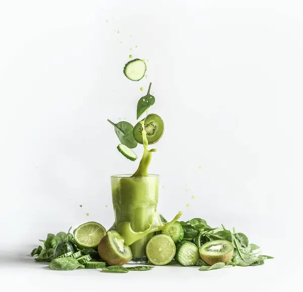在玻璃杯中洒上绿色的冰沙 配以飞扬的配料 猕猴桃和菠菜叶 背景为白色 有大量的绿色水果和蔬菜 健康清爽的饮料 免版税图库照片