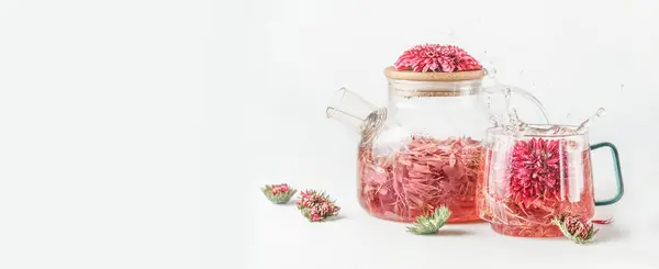 白い背景に液体を飛ばすガラス鍋とカップにピンクの花が付いているハーブティー 風味のある健康的な飲み物のコンセプト フロントビュー バナー ストック画像
