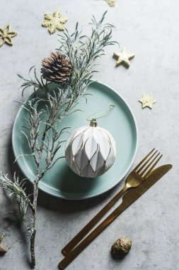 Tabaklı Noel masası seti, altın çatal bıçak, dekorasyon ve köknar yeşillikleri, yıldızlar ve mücevherler beton zeminde. Şenlikli yemek geçmişi. Üst görünüm.
